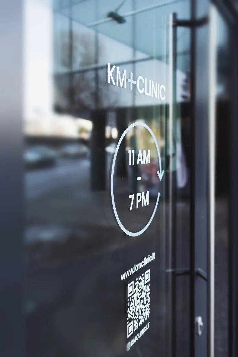 KM+CLINIC įėjimo durys su iškaba ir darbo laiku